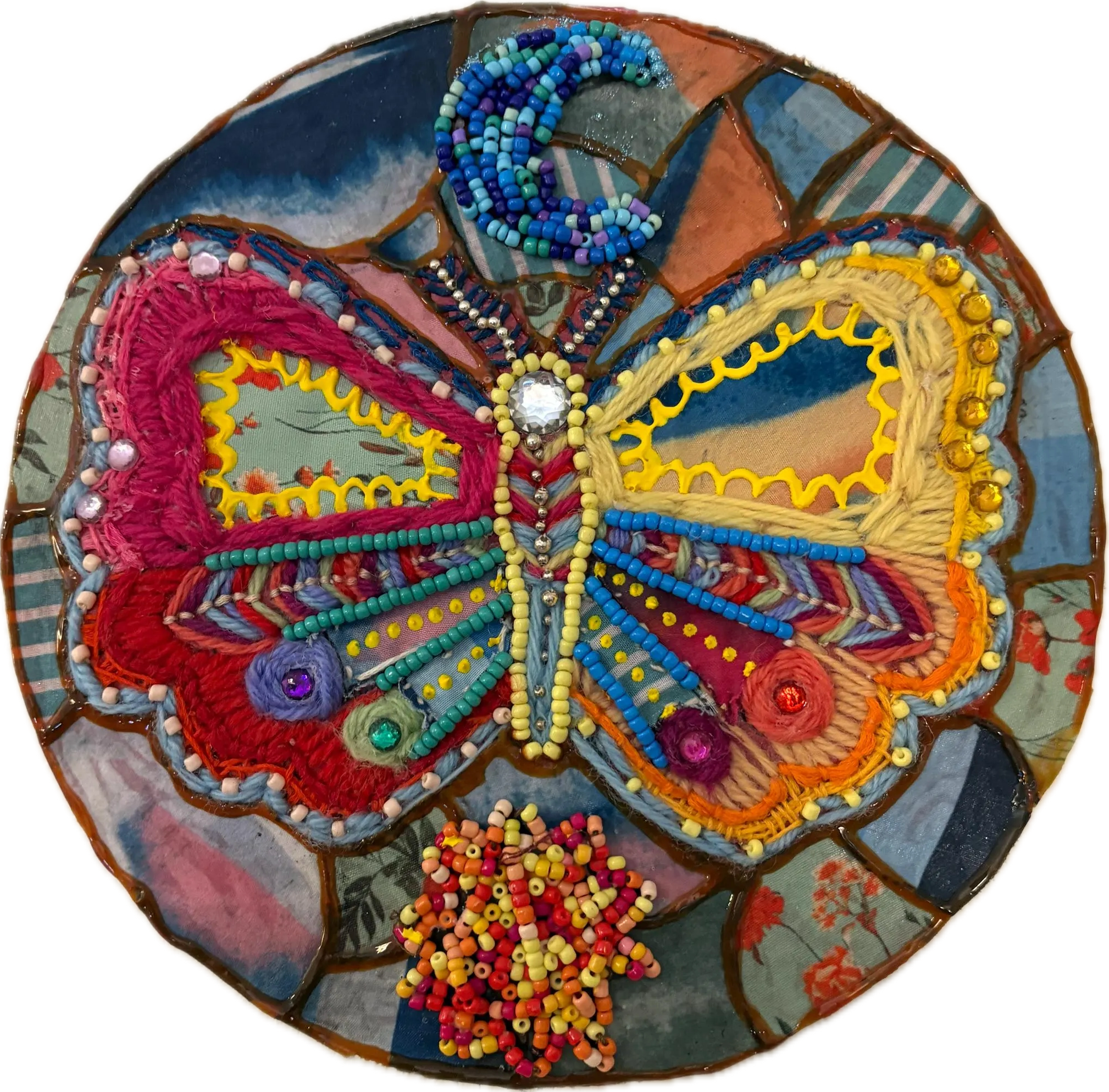 A colorful handmade mosaic made with various beads, embroidery, and fabric pieces, featuring a swirl pattern with colors like blue, red, yellow, purple, and white.