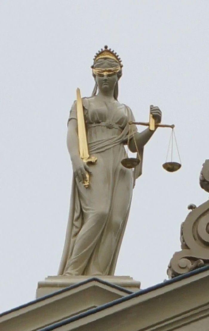 Statue of Lady Justice holding a scale and sword, wearing a blindfold, with gold accents on the sword handle and the scales.