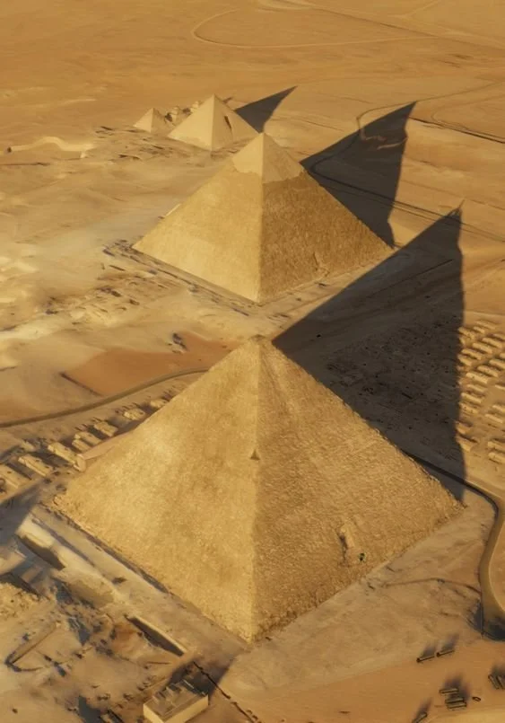 Three pyramids made of beige stones or sand, arranged in a row on a desert landscape with tire tracks and shadows.