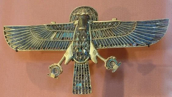 A metallic sculpture of a mythological creature with outstretched wings, holding objects in each talon, mounted on a wall.