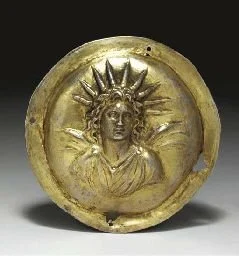 Gold-colored circular medal with a relief of a woman wearing a crown of rays, representing the Statue of Liberty, on a black background.