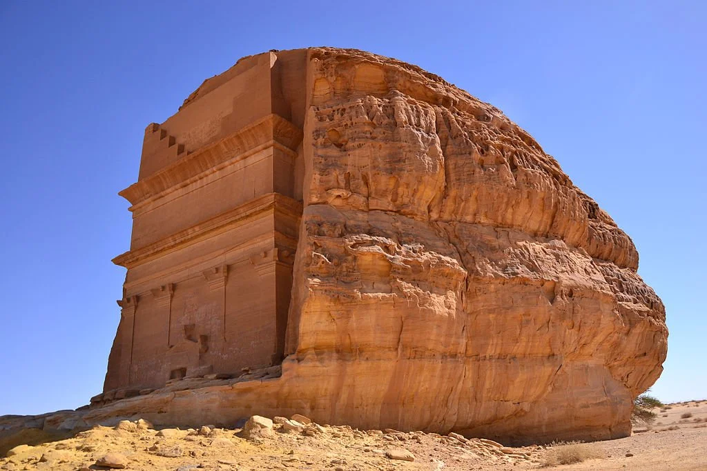 A large stone structure with ancient carvings on a desert landscape against a clear blue sky.