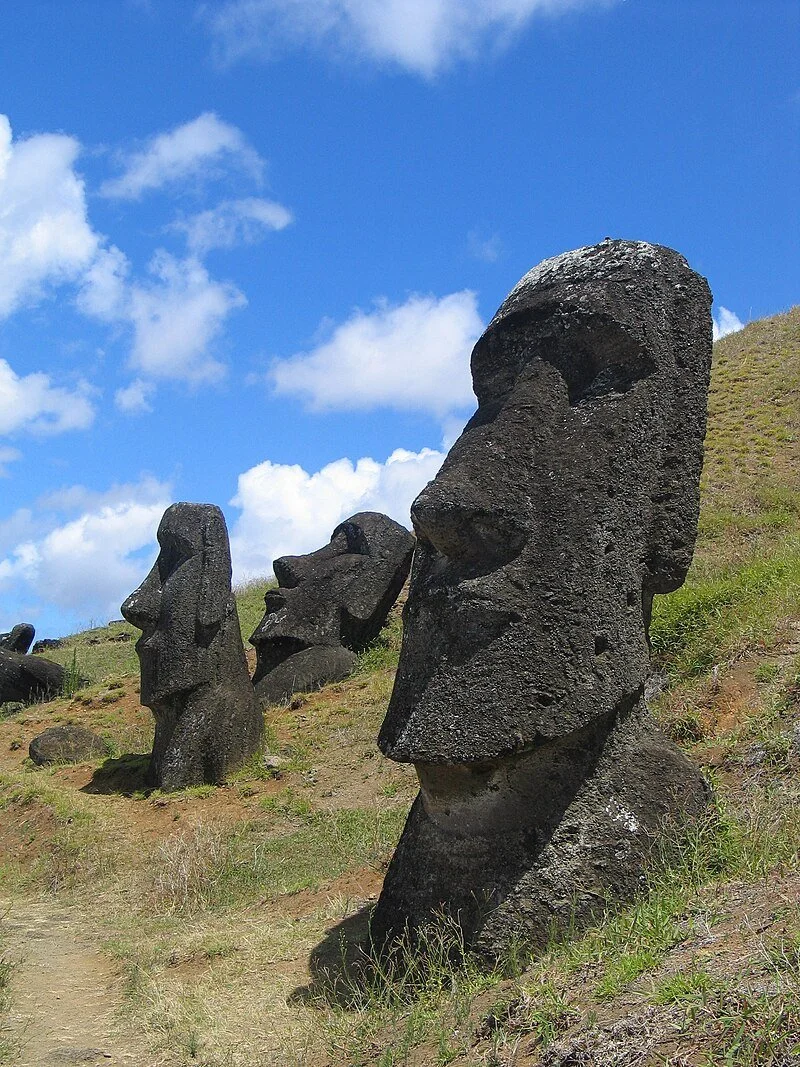 Three large Moai statues on a grassy hillside under a partly cloudy blue sky.
