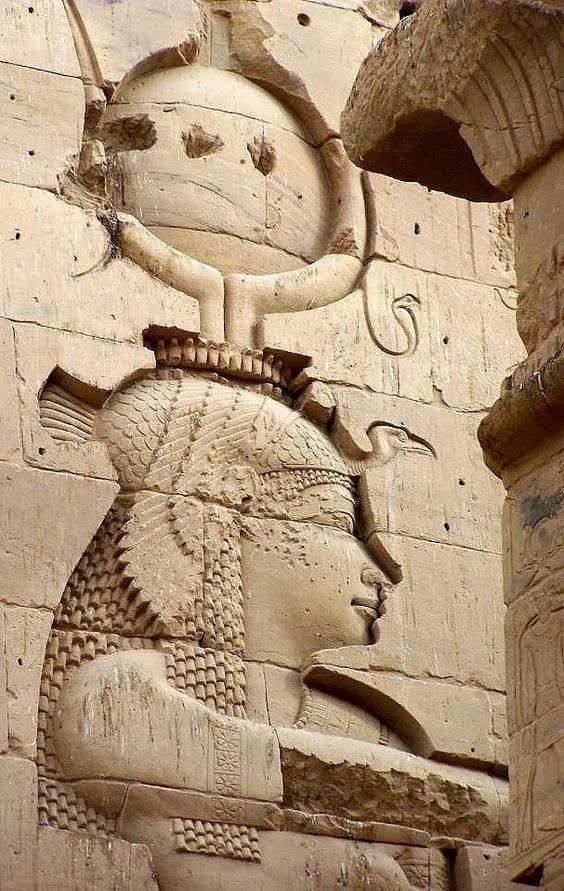 Ancient stone relief of an Egyptian goddess with a headdress and a sun disk, carved into a wall.
