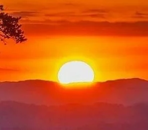 Sun setting over mountain range with a colorful orange and yellow sky.