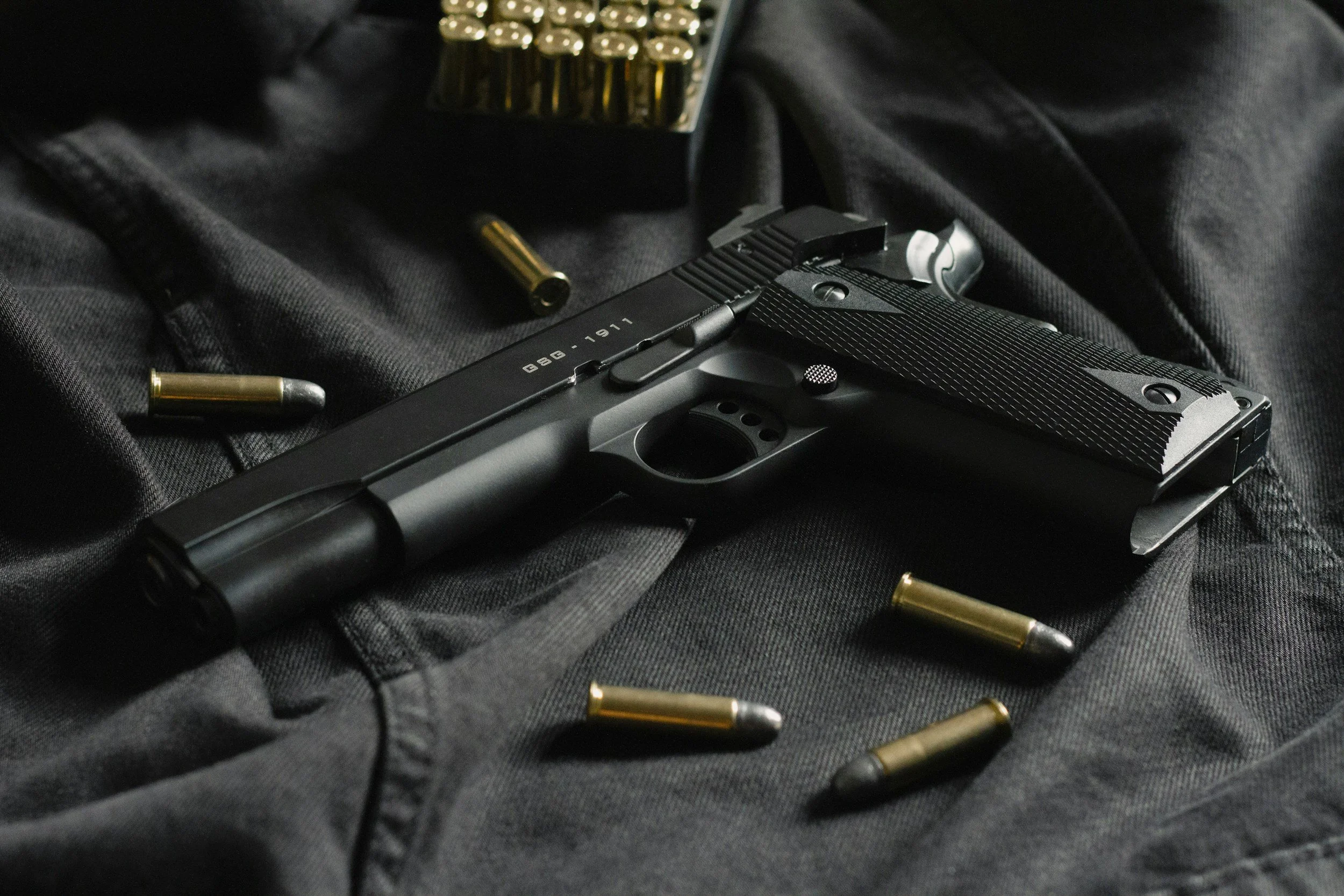 A semi-automatic handgun lying on a dark fabric surface with spent brass casings and shotgun shells scattered around it.