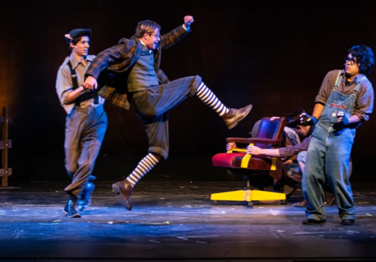 Actors performing on stage in a theatrical production, with one person mid-air and others holding props and seated. Jed Johnson plays Toad in “Wind in the Willows.”