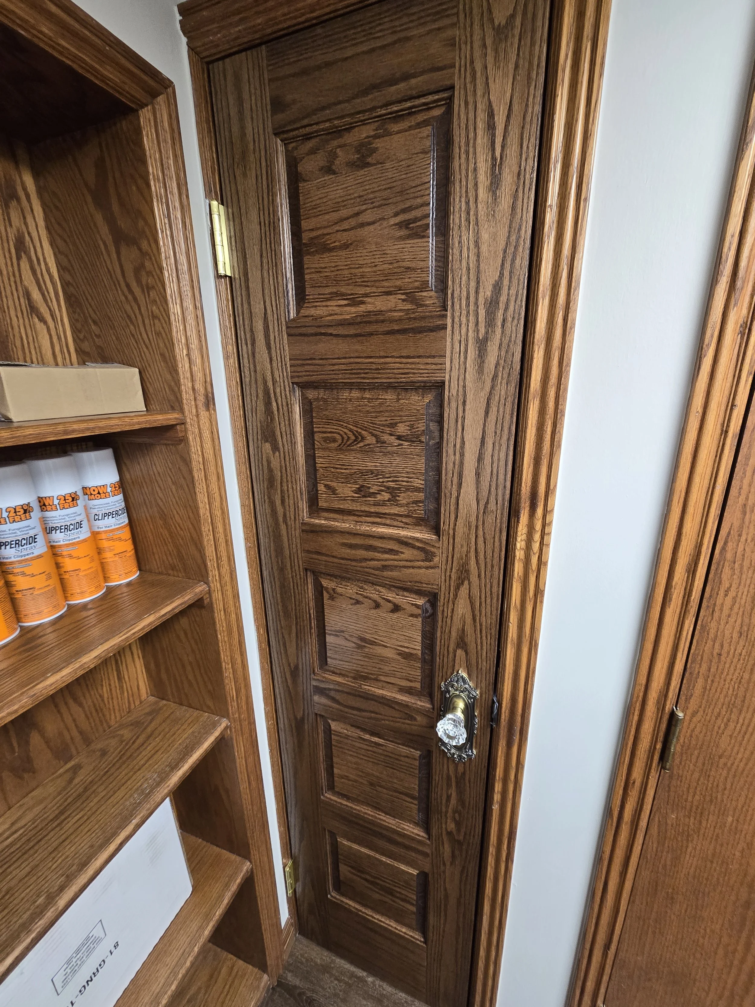 A wooden closet door with a decorative handle, surrounded by wooden shelves with some paint cans and a cardboard box.