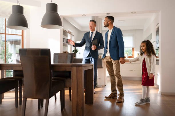 Two men and a young girl in a bright, modern kitchen. One man is holding a tablet and gesturing, while the other man is holding the girl's hand.