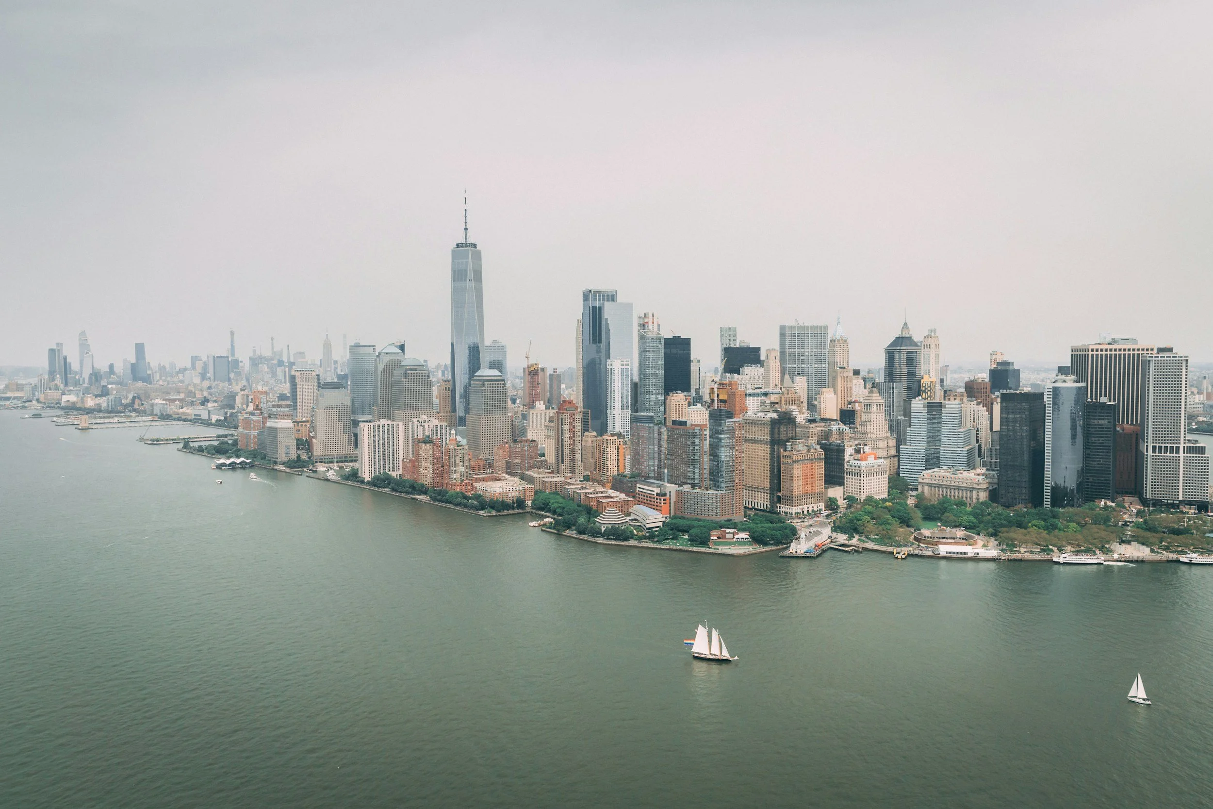 Aerial view of Manhattan skyline with skyscrapers, waterfront, and sailboats on the water.