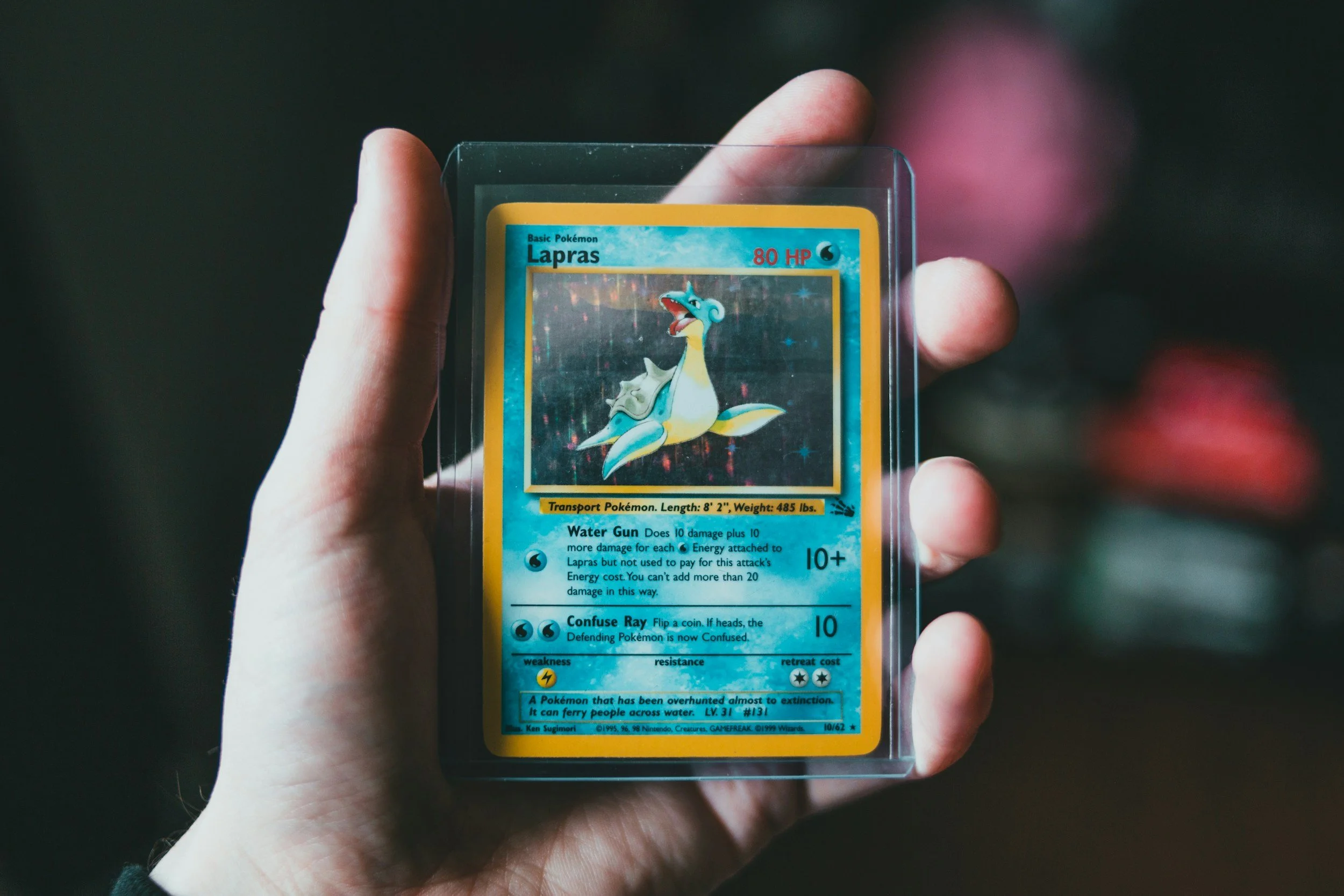 A person holding a vintage Pokémon trading card of Lapras in a protective plastic case. The card features Lapras' illustration, its name, health points, and attack details.