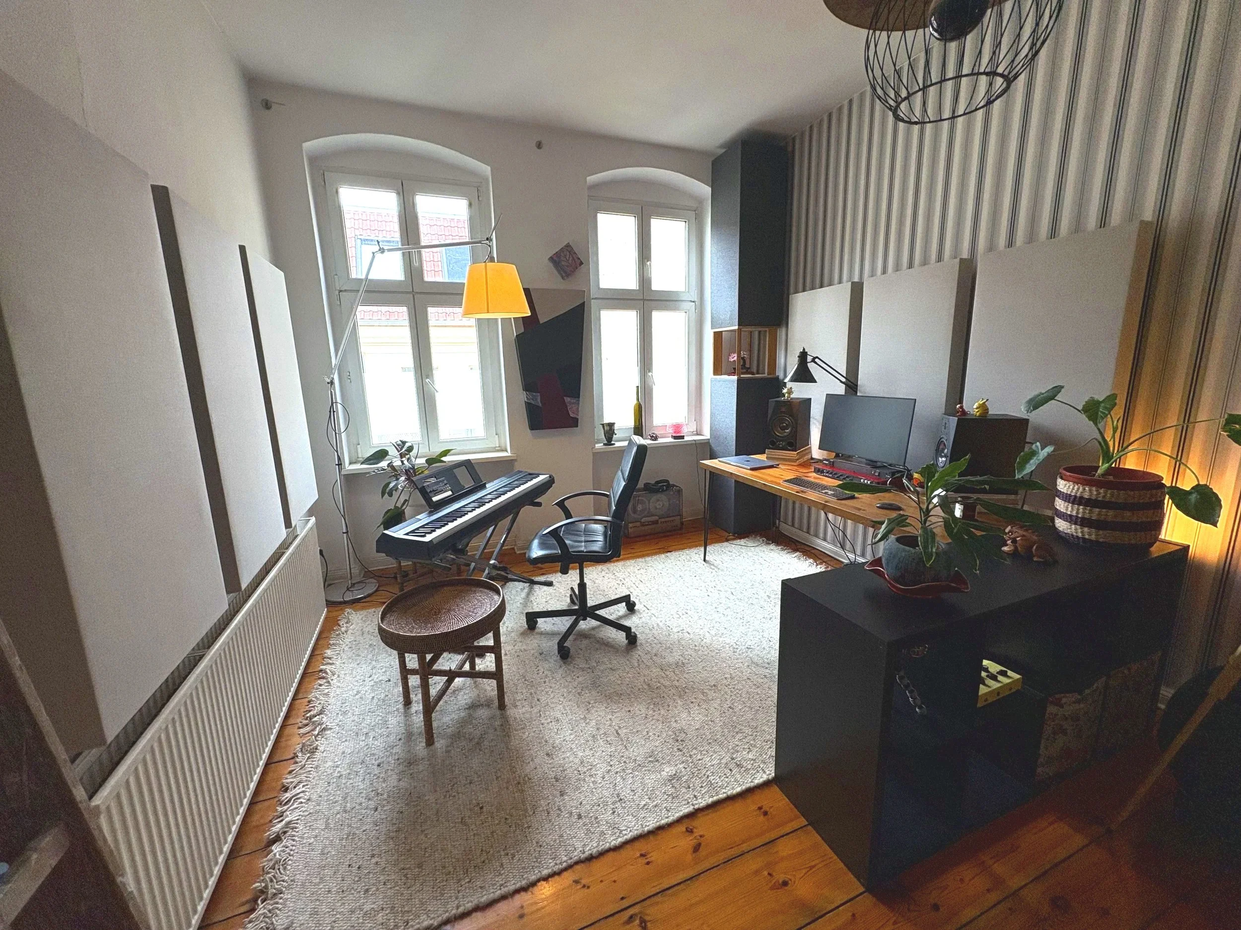 Gemütliches Zimmer mit großen Fenstern, einem Klavier, einem Computer und Pflanzen. Dekorative Wandpaneele, Lampen, Stuhl und Teppich
