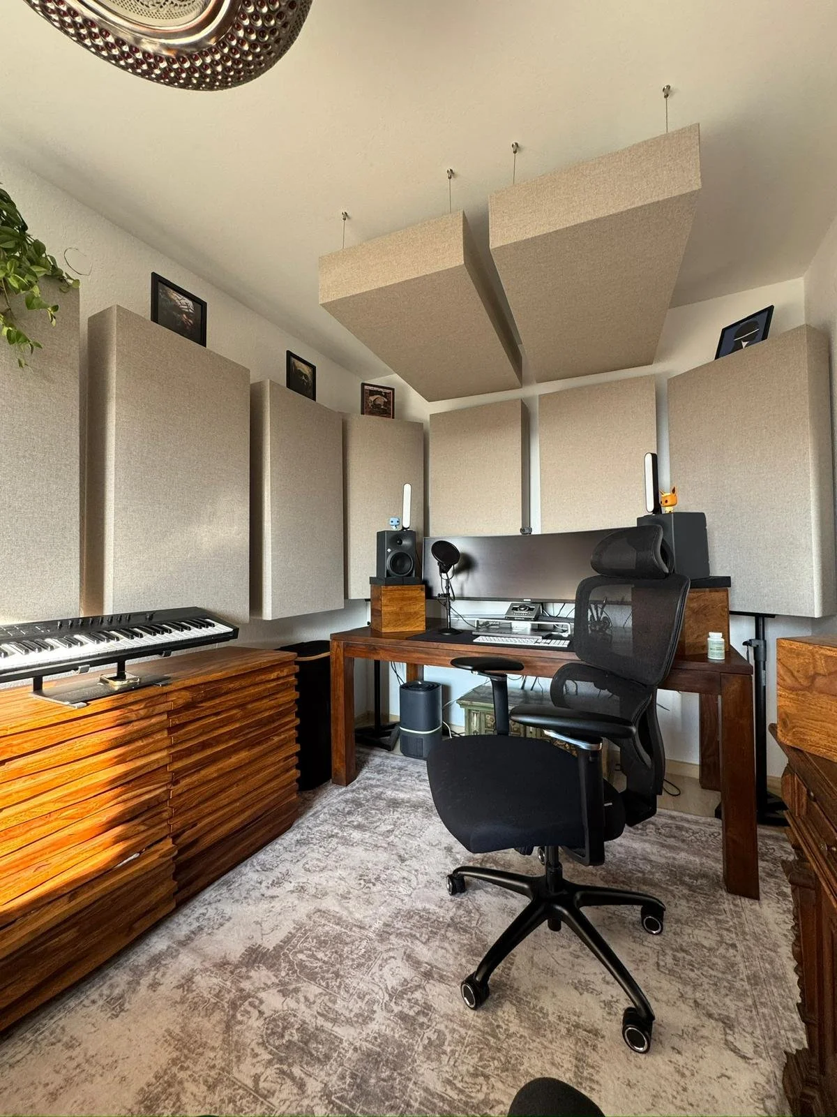 Musikproduktionsraum mit Piano, Schreibtisch, Monitor, Regale und akustische Wandpaneele sowie Schallplatten und Pflanzen.