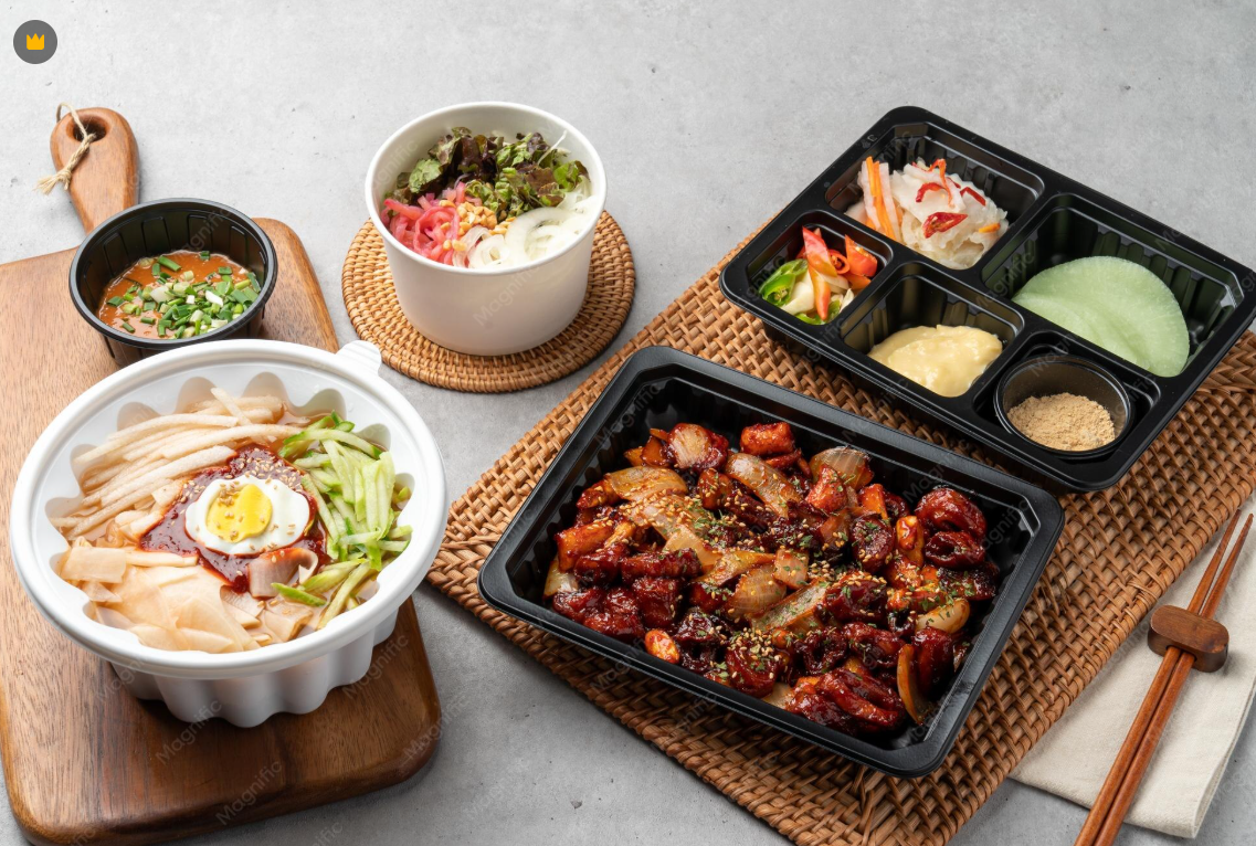 Korean meal with rice, vegetables, and spicy meat, accompanied by salad, soup, and side dishes on a gray surface.