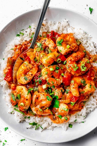 A bowl of shrimp and vegetables served over white rice, garnished with chopped green onions.