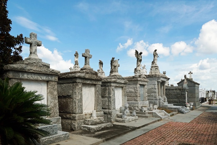 Row of old stone tombs with crosses and statues in a cemetery under a blue sky.