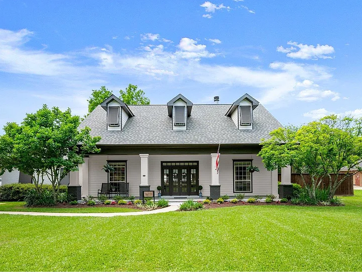 Front view of a modern house with a gray roof, white walls, and black window frames, surrounded by green lawns and trees under a blue sky.