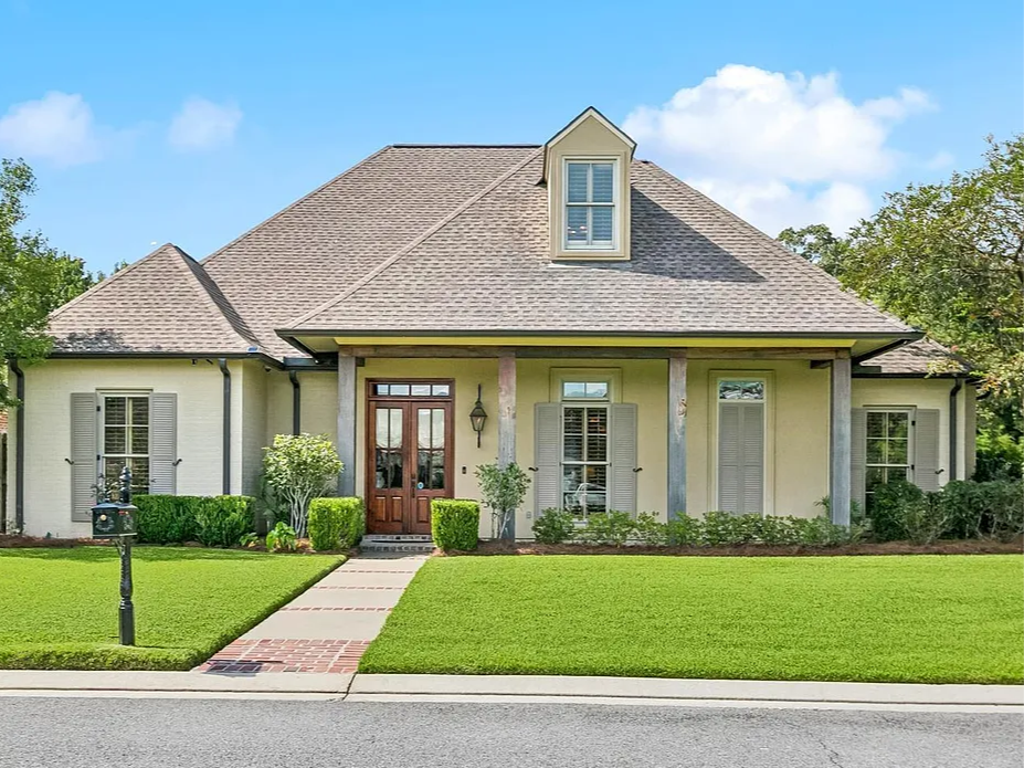 A house with a front yard, green grass, a brick sidewalk, bushes, and a mailbox