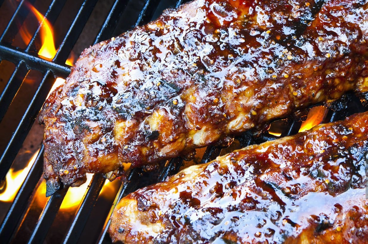 Barbecue ribs being grilled on a barbecue grill with flames visible underneath.