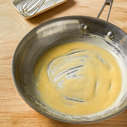 Empty or nearly empty frying pan with some remnants of yellow batter, on a wooden surface.