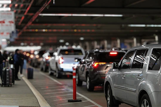 Line of cars parked under an airport terminal with luggage and people nearby.