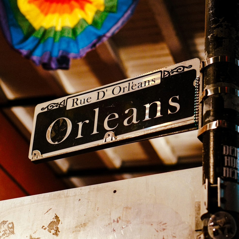 Street sign reading 'Rue D'Orleans' and 'Orleans' attached to a pole, with a rainbow-colored paper decoration in the background.