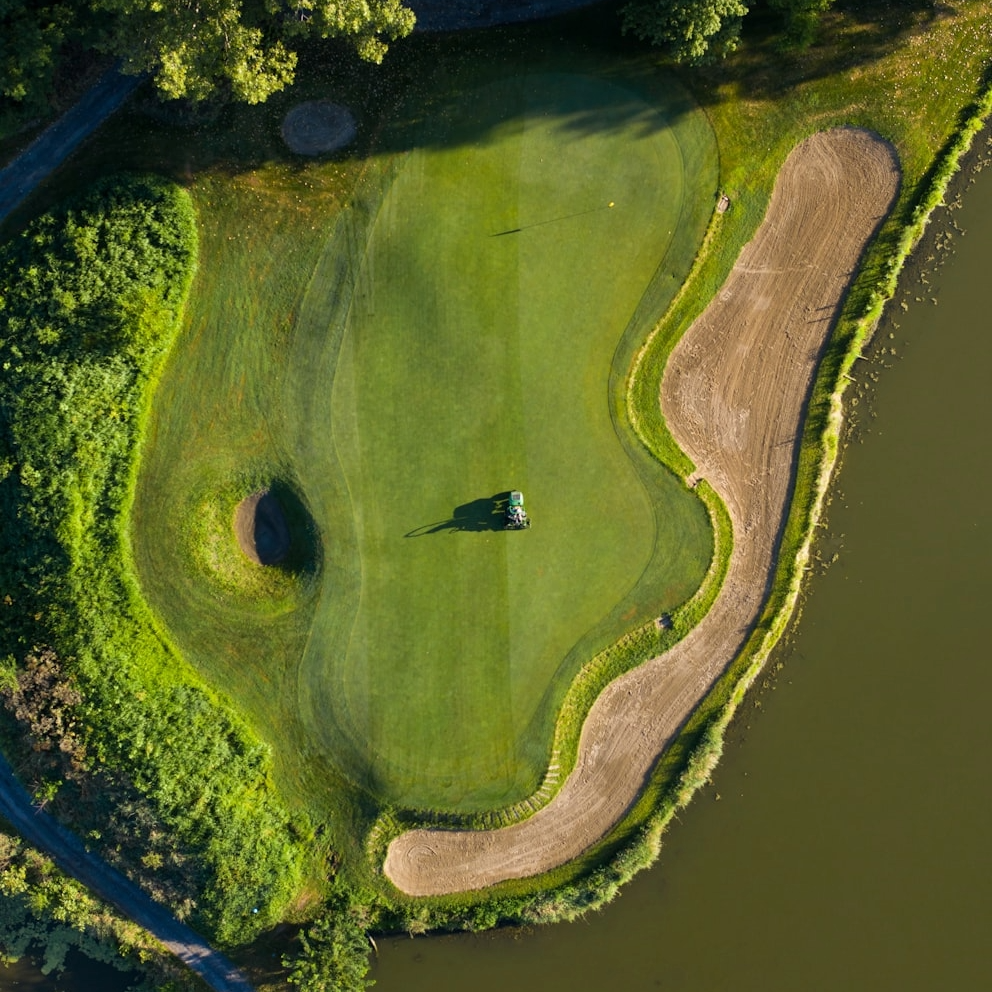 Aerial view of a golf course putting green surrounded by sand traps, water, and trees.