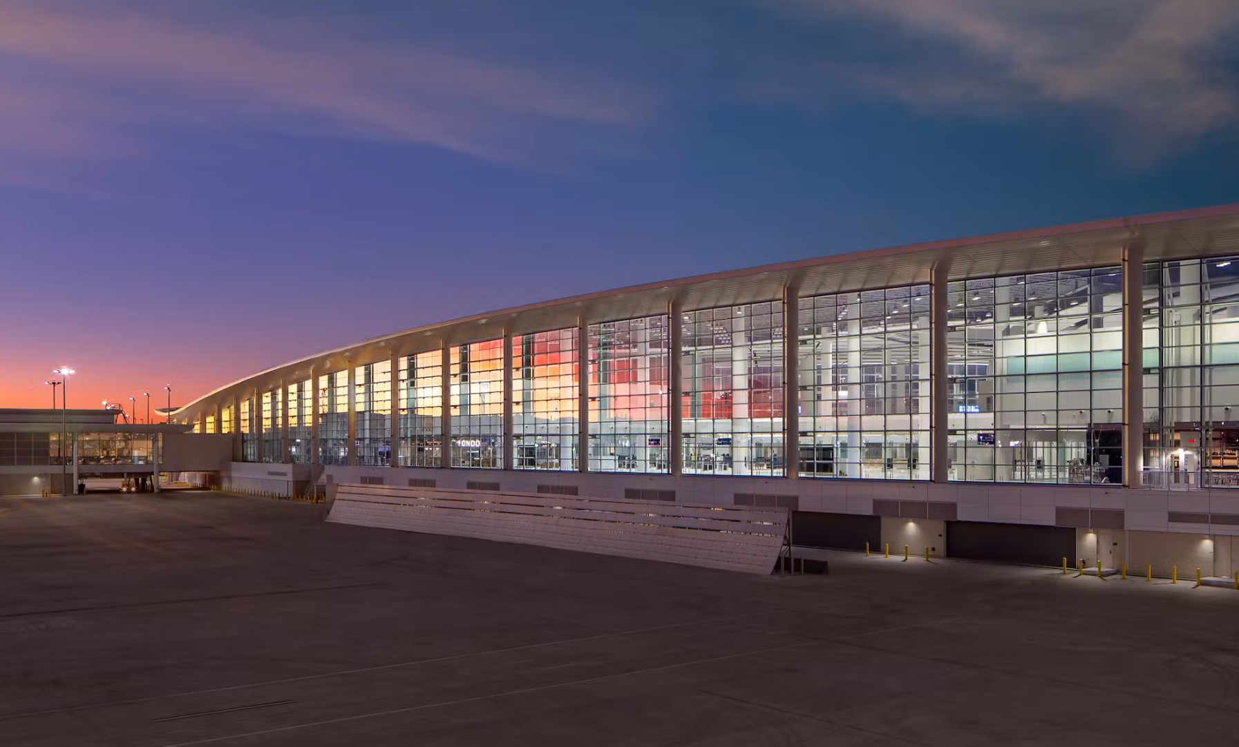 Modern airport terminal building with large glass windows illuminated from within at sunset