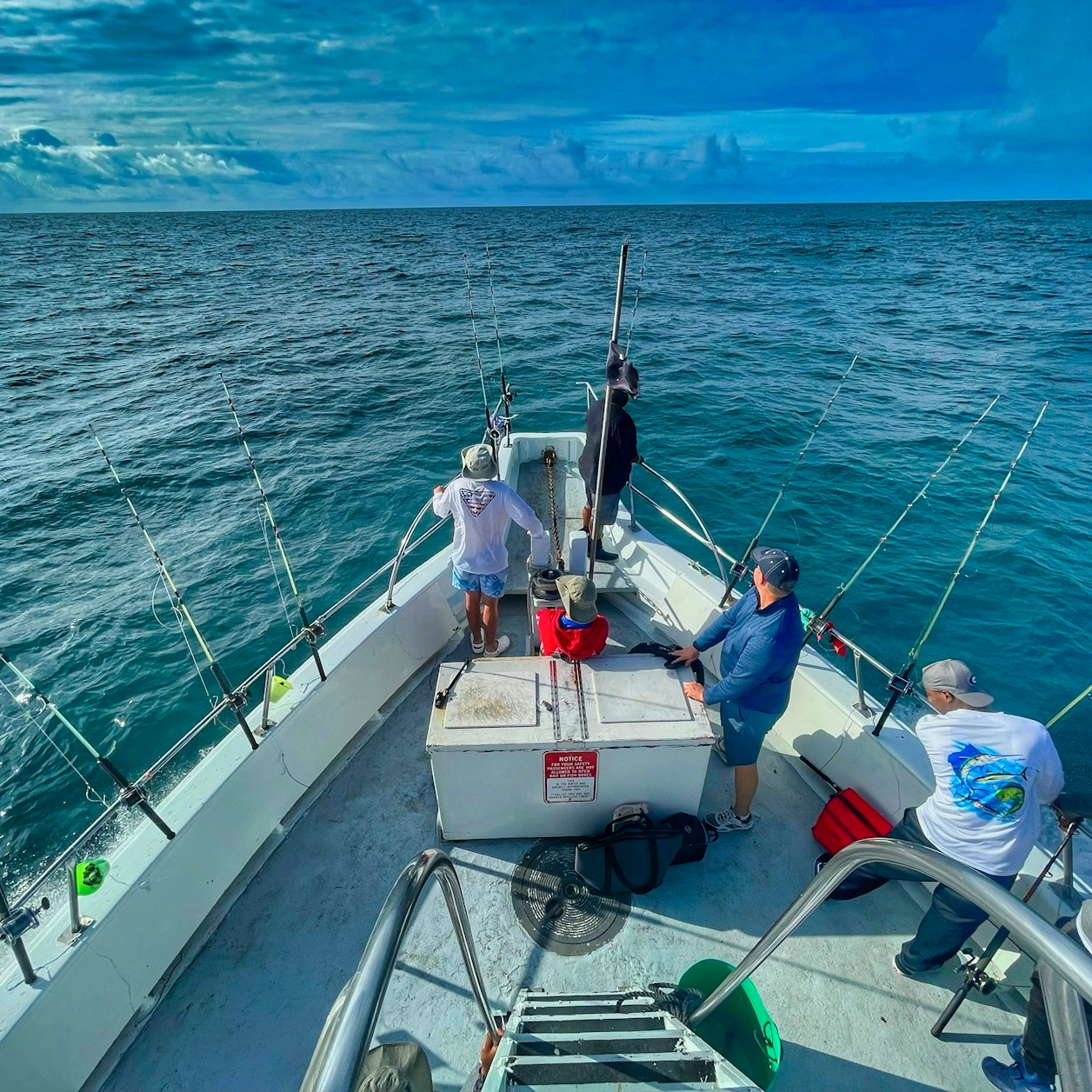 Several people on a boat fishing in the open ocean with a cloudy sky overhead.