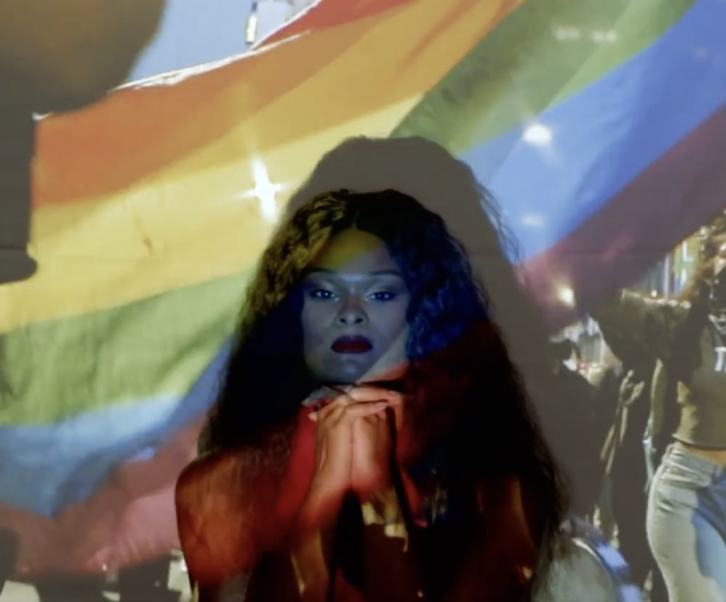 Still from PRIDE documentary series featuring a Black trans woman with an LGBTQ pride flag projection, edited by Genea Gaudet
