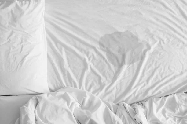 Un unordentliches weißes Bett mit heruntergelassener Bettdecke und einem Kissen auf der linken Seite.
