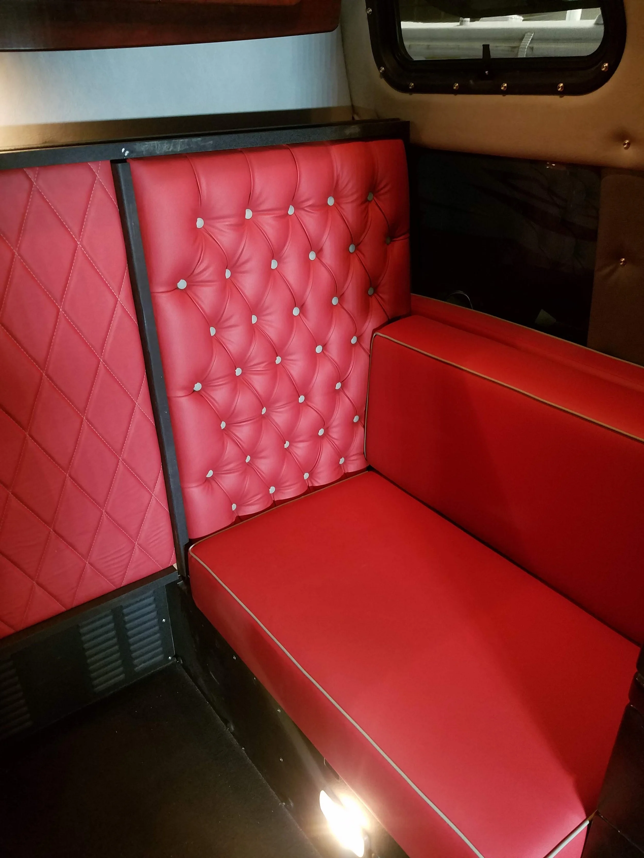 Interior of a vehicle with red cushioned seating and a window showing an outdoor scene.