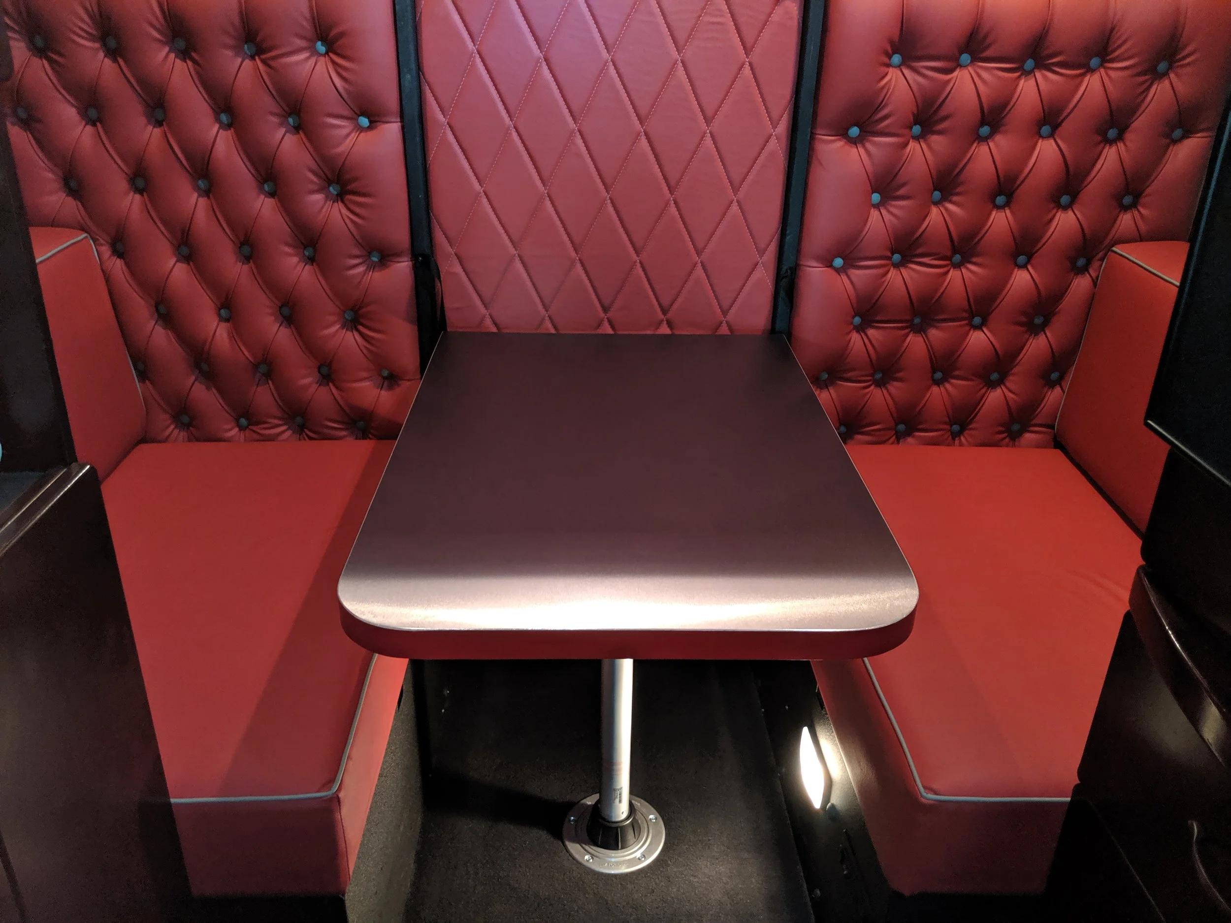 Red upholstered booths with diamond-patterned padding and a centered table with a metal pedestal base, set in what appears to be a restaurant or cafe seating area.