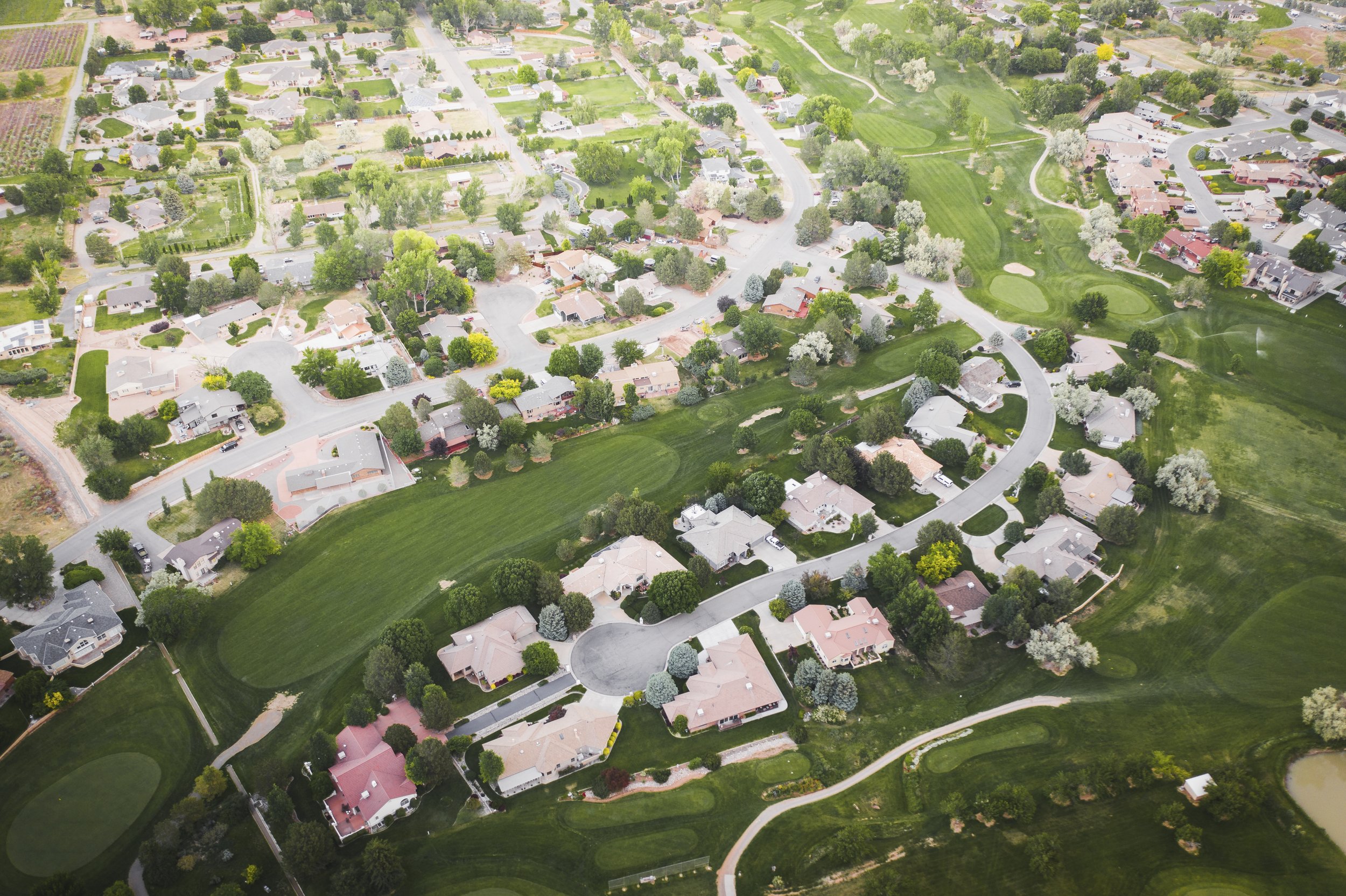 Aerial view of a residential neighborhood with houses, trees, and golf course greens.