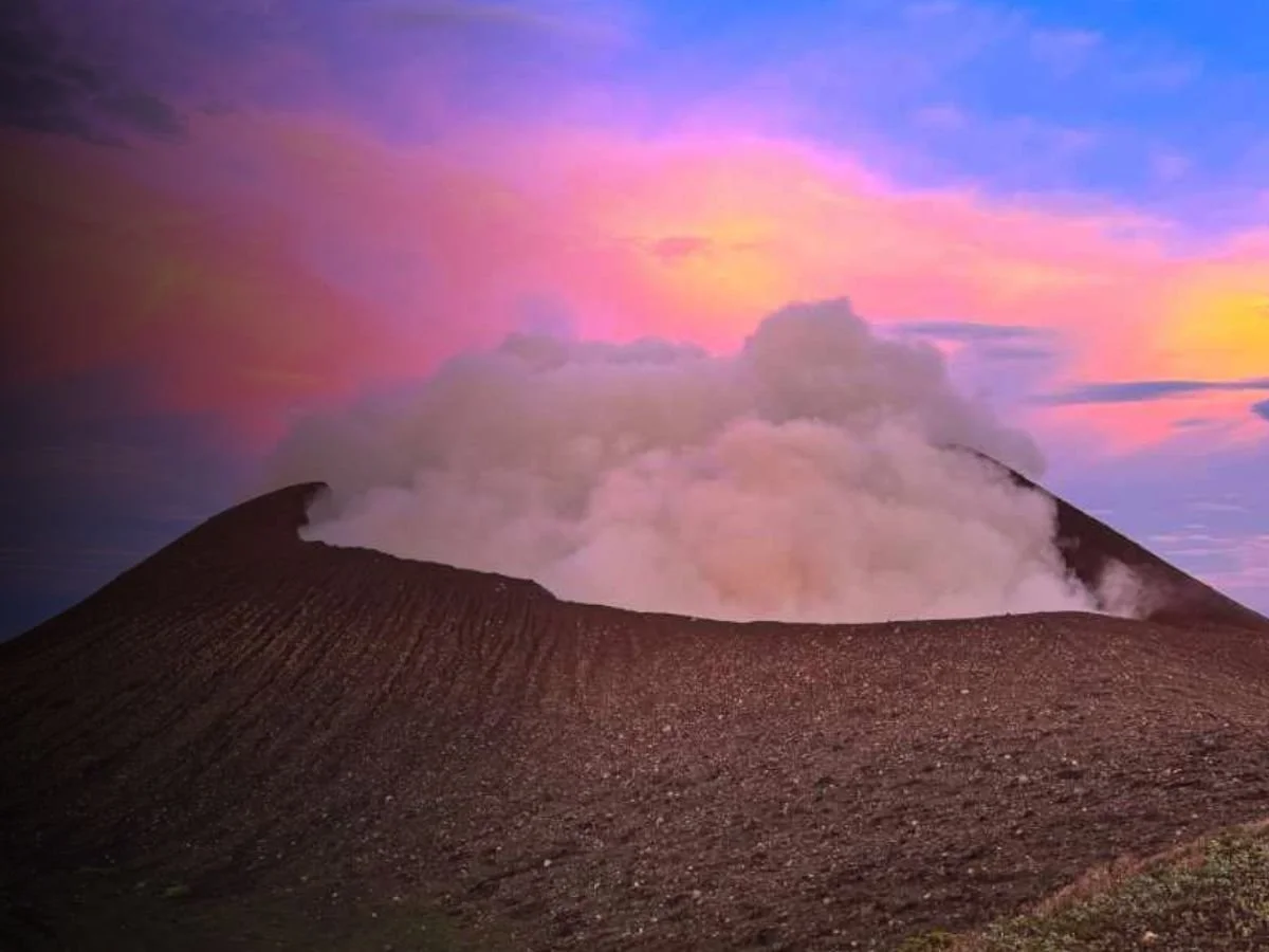 Volcano erupting with smoke and ash under a colorful pink, purple, and orange sky.