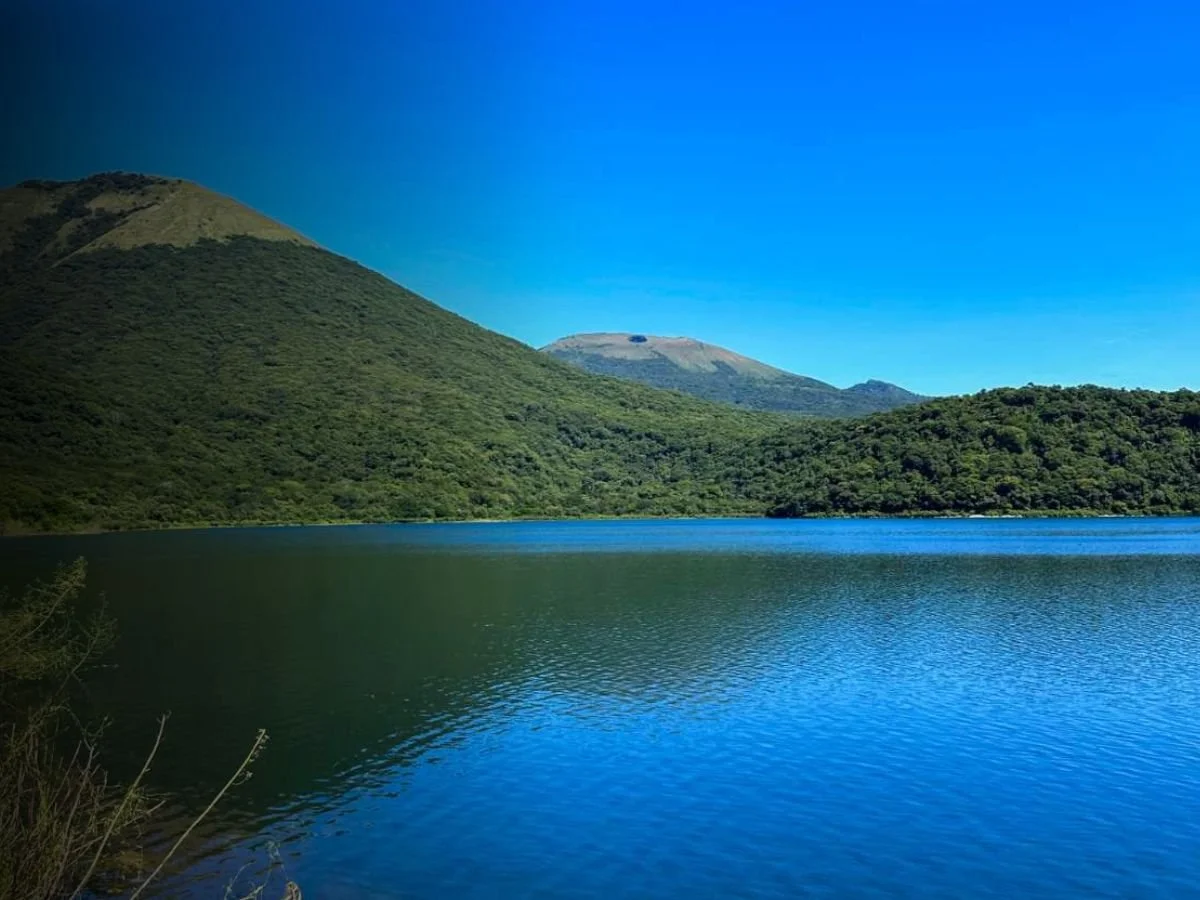 A lake with green hills and mountains in the background under a clear blue sky.