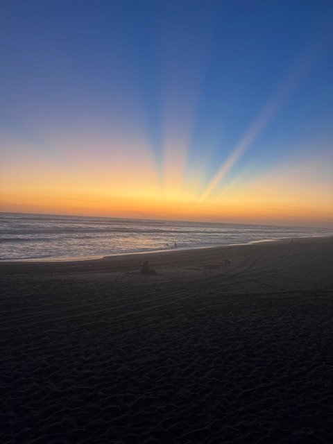 Las Penitas sunset over the ocean with colorful rays in the sky and a sandy beach in the foreground.