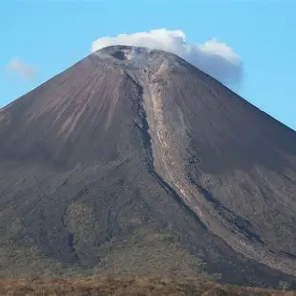 A volcanic mountain with a small cloud near the summit and a visible lava flow down the side.