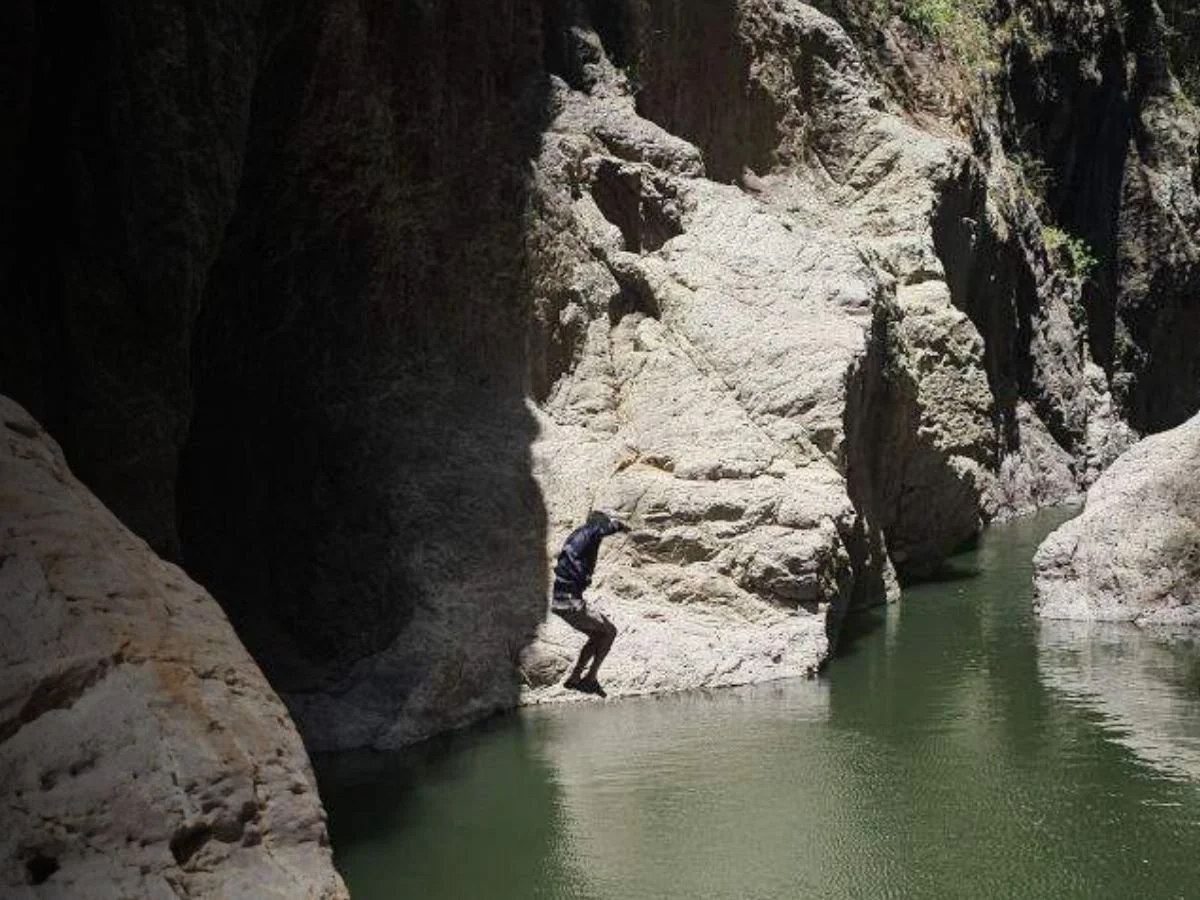 Person climbing on rocks beside a green river in a rocky canyon.