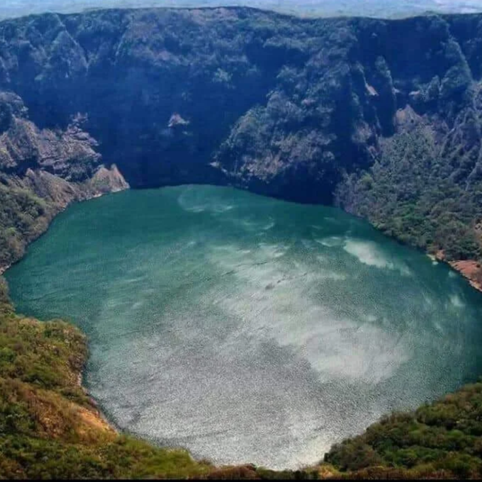 A volcanic crater lake surrounded by steep, forested cliffs.