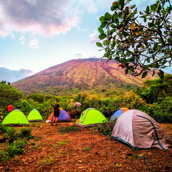 Tents set up in a campsite with a volcano in the background and a few people nearby.