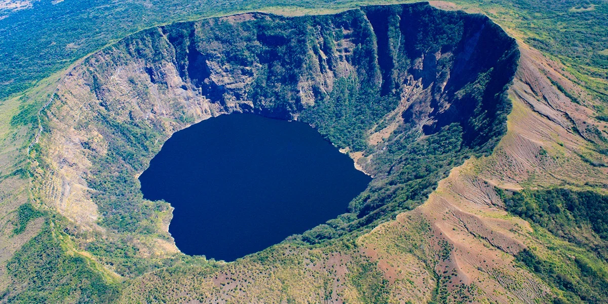 Cosiguina volcanic crater lake surrounded by steep, vegetated slopes with visible lava flows and lush green vegetation around.