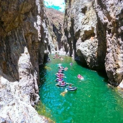 People in inner tubes floating through a narrow, rocky canyon with green water.