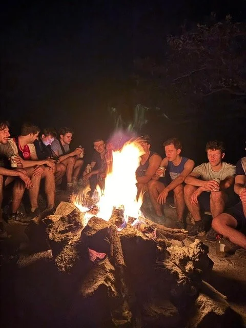 Group of young people sitting around a campfire at night.