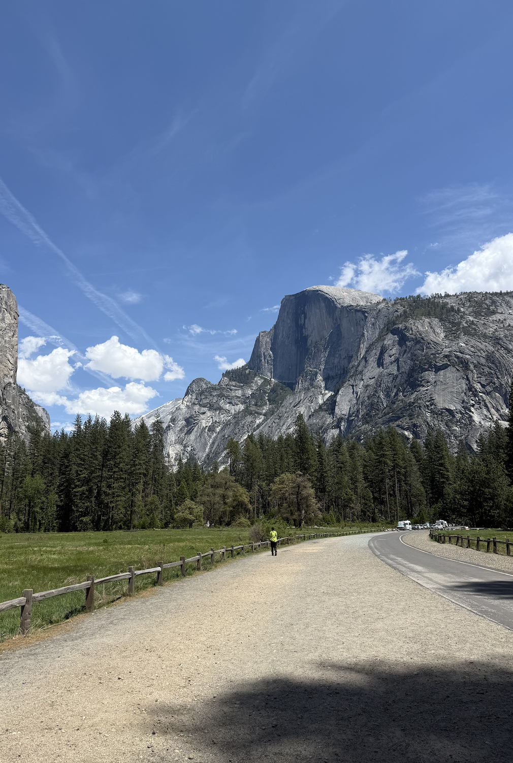 Scenic view of a pathway leading towards iconic Half Dome in Yosemite National Park with lush green trees and a clear blue sky.