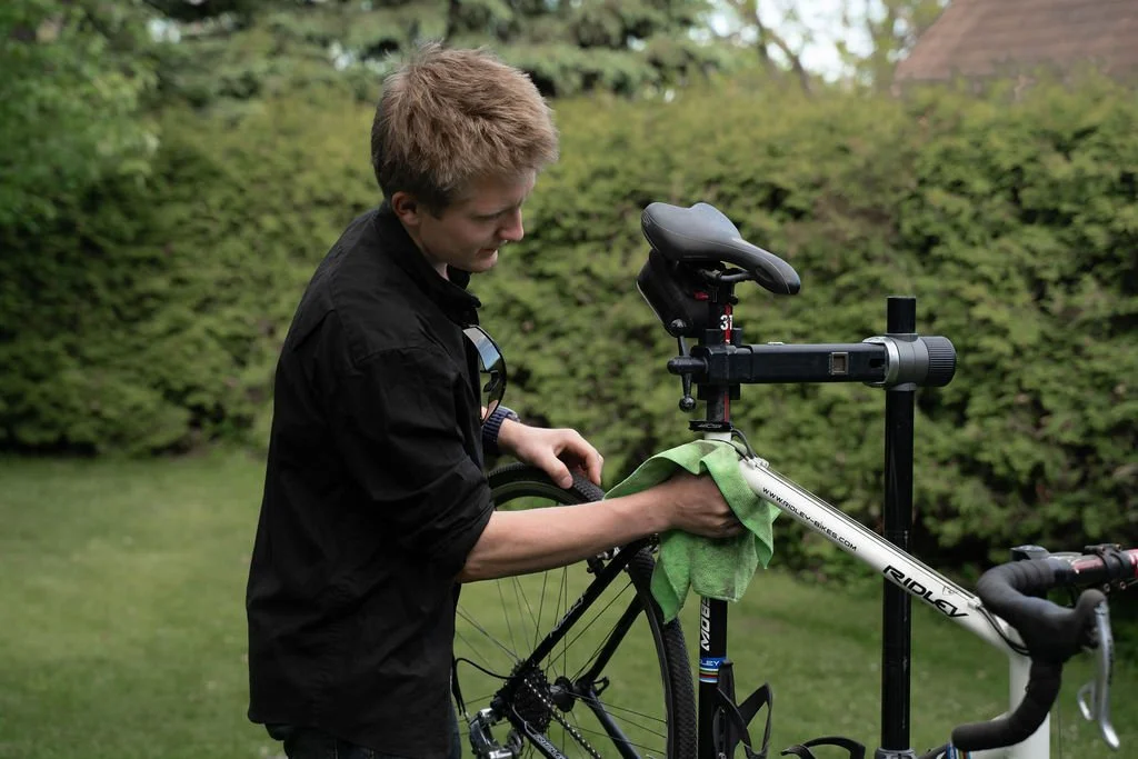 A person cleaning a bicycle with a green cloth outdoors.