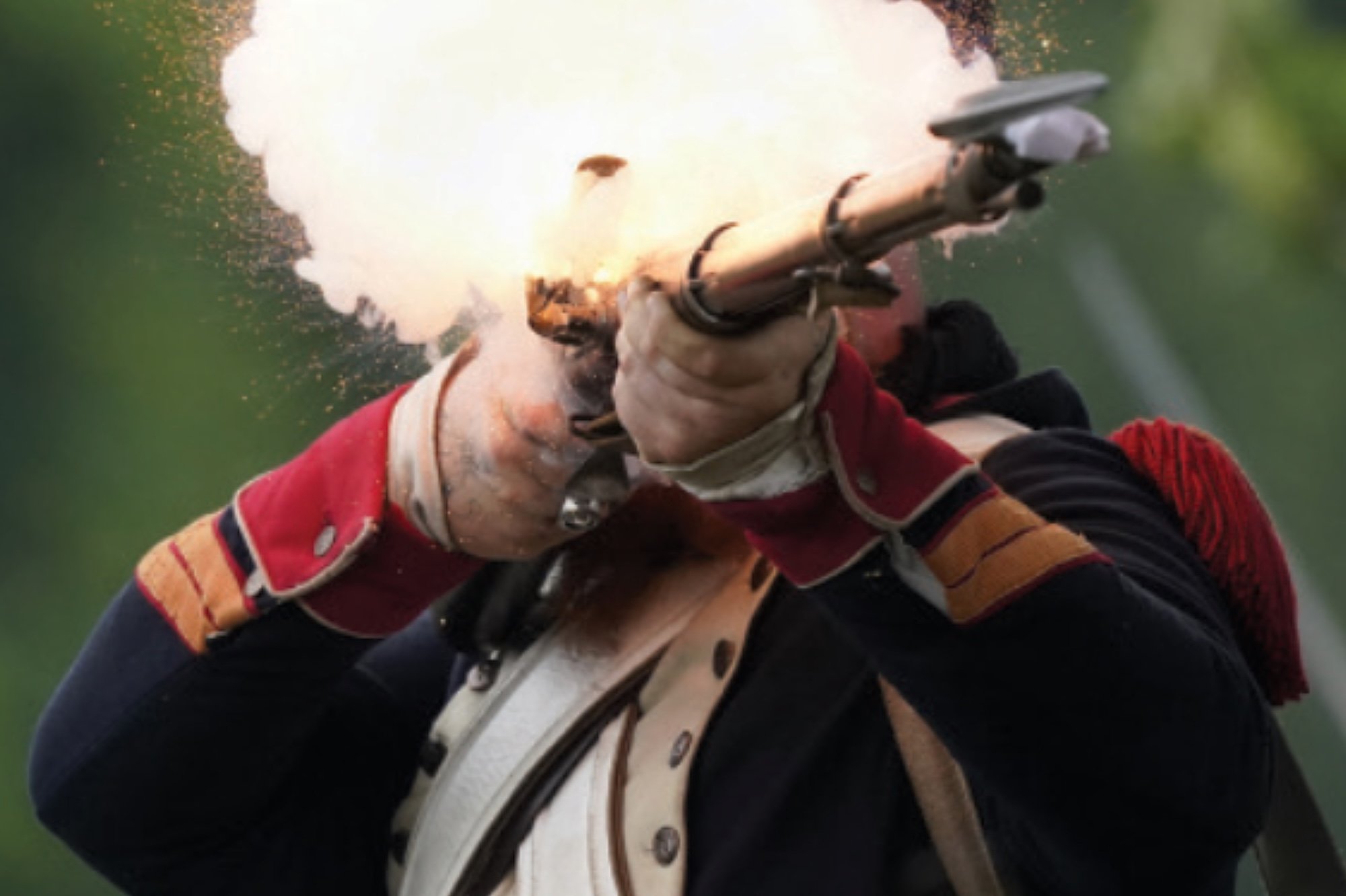 A person wearing a red, beige, and black striped jacket and a tan vest is firing a gun, which is creating a muzzle flash and smoke.