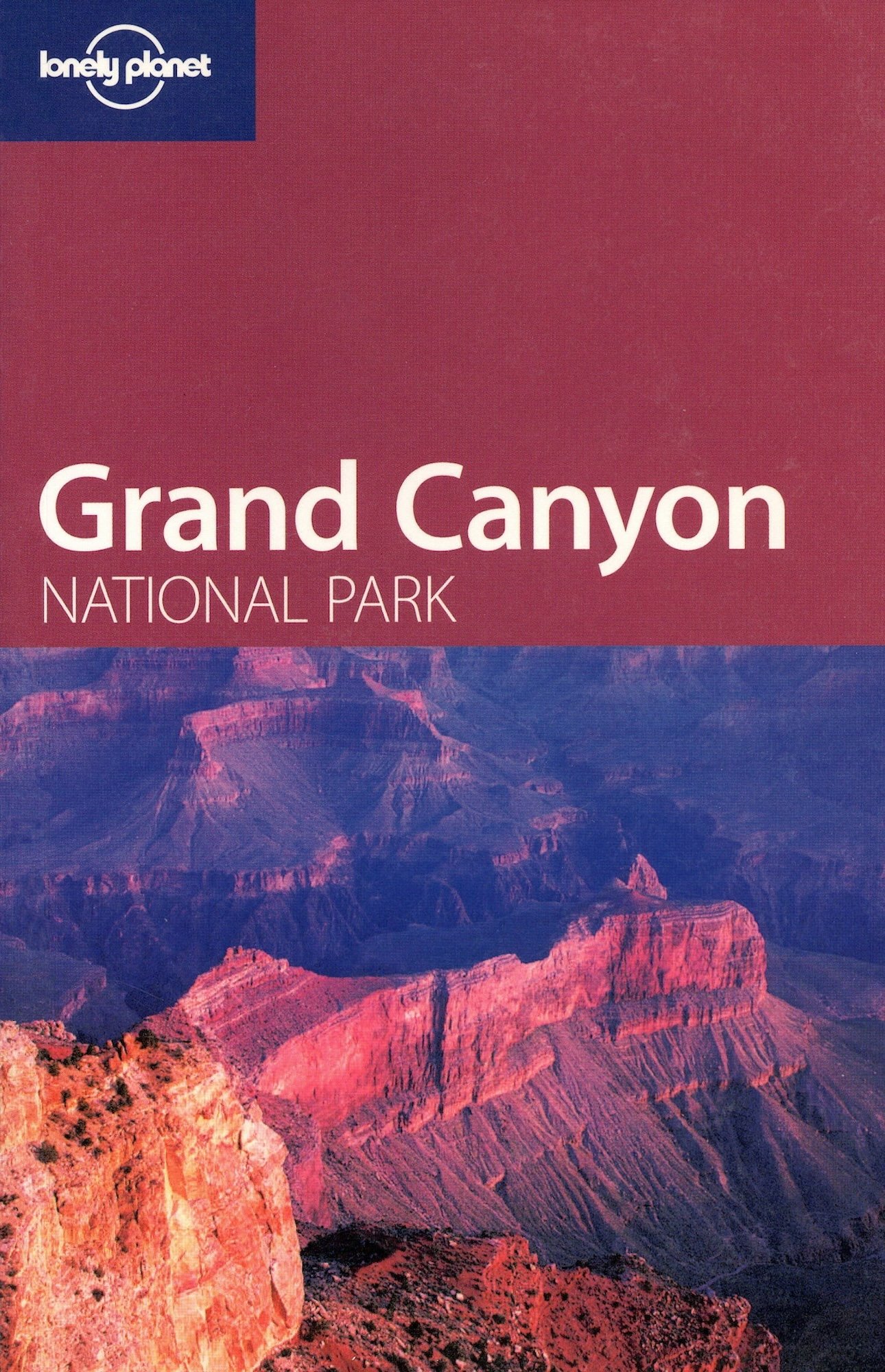 A scenic view of the Grand Canyon with layers of red and purple rock formations, under a clear sky. The image is the cover of a travel guide for Lonely Planet.