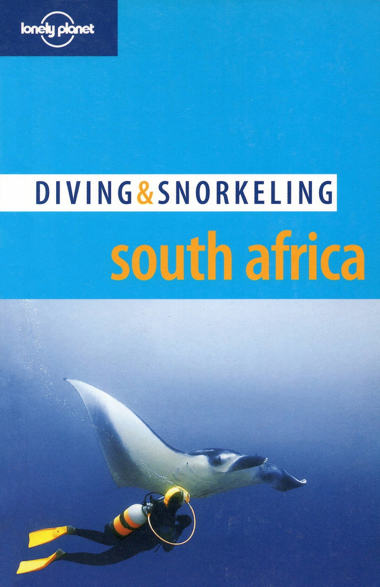 The cover of Lonely Planet's diving & snorkeling guide to South Africa. A diver with yellow fins, a diving suit, and a scuba tank swimming near a great white shark in the ocean.