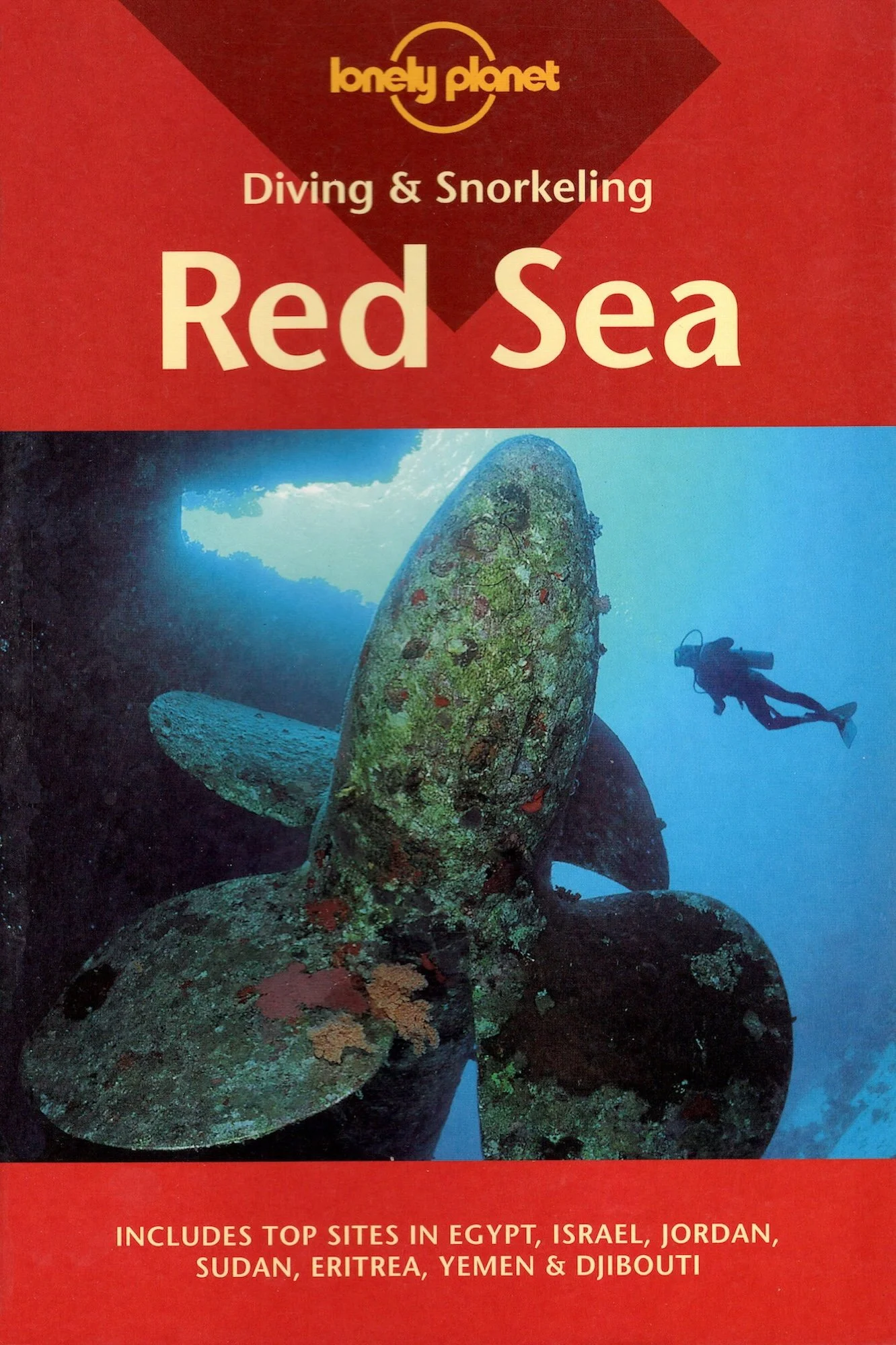 Lonely Planet's diving & snorkeling guide to the Red Sea. A scuba diver explores underwater ruins covered in colorful coral and sponges, with large stone anchors in the foreground and a dark underwater cave in the background.